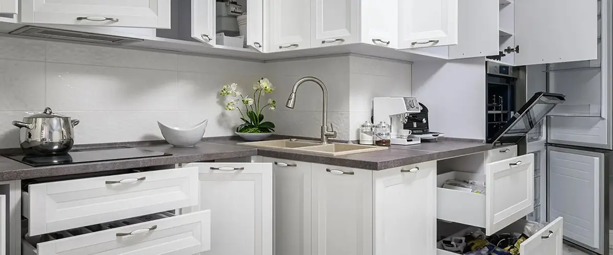 Compact kitchen with white cabinets and open drawers around the sink area