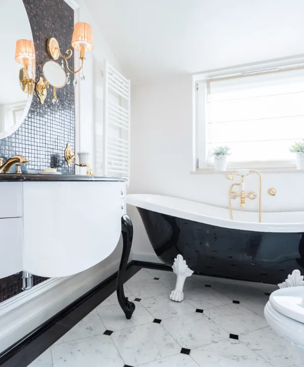 Elegant bathroom featuring a vintage black clawfoot tub, white cabinet, gold fixtures, and stylish decor with marble flooring.