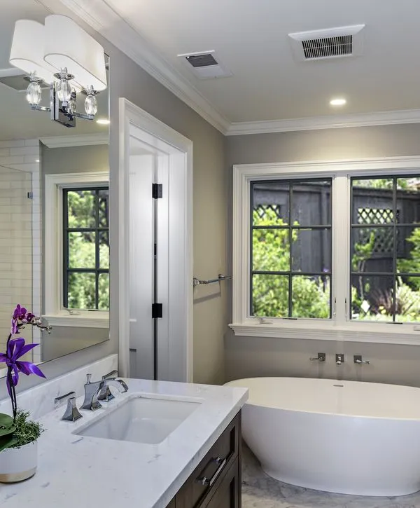 Contemporary bathroom featuring a dark wood vanity with white marble counter, a freestanding white tub under windows, and purple orchid decor