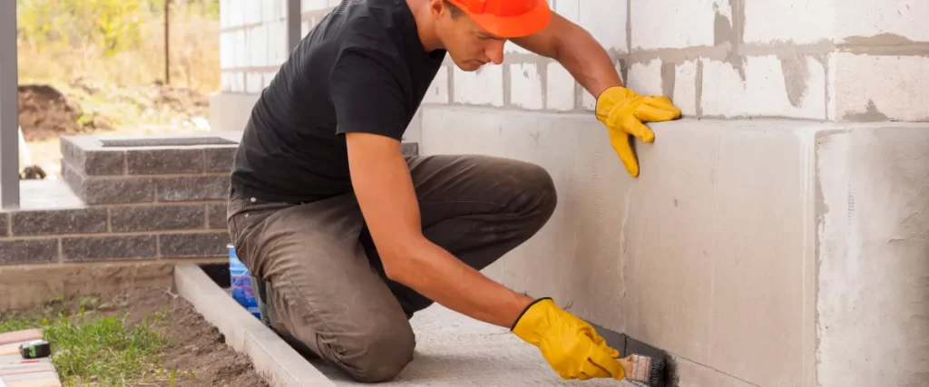 a worker applying a masonry waterproof coating to a concrete foundation or wall