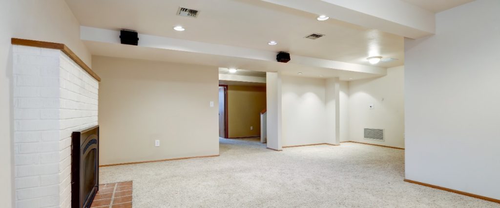 an unfurnished basement features a carpeted floor, white painted walls, and a white brick fireplace with a dark insert