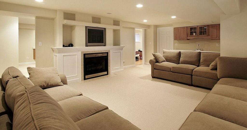 A beautifully remodeled basement living room featuring a modern fireplace, cozy beige sofas, and recessed lighting. This space is perfect for entertaining or relaxing in a well-designed basement.