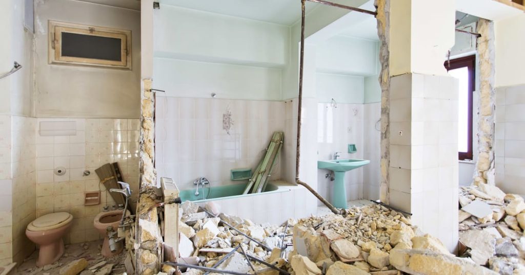 A bathroom demolition in progress showing a pile of concrete rubble, broken tiles, and an old green bathtub in a partially gutted room.