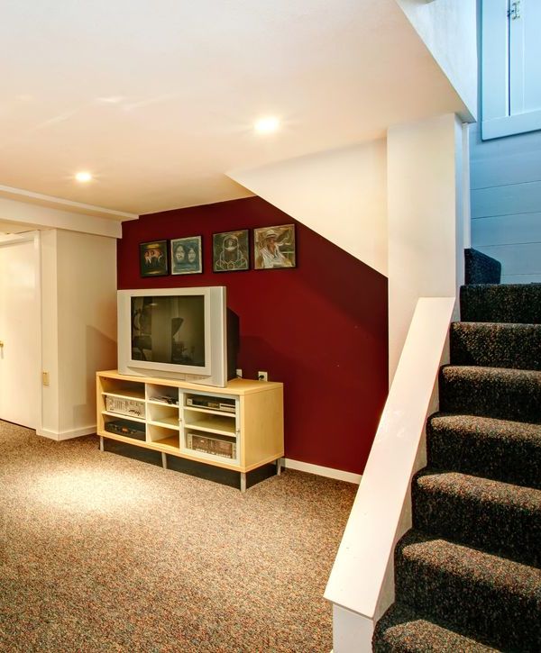 A beautifully finished basement remodeling project featuring contemporary gray sofas, a white coffee table, a tall potted plant, and a wide horizontal egress window that provides natural light.