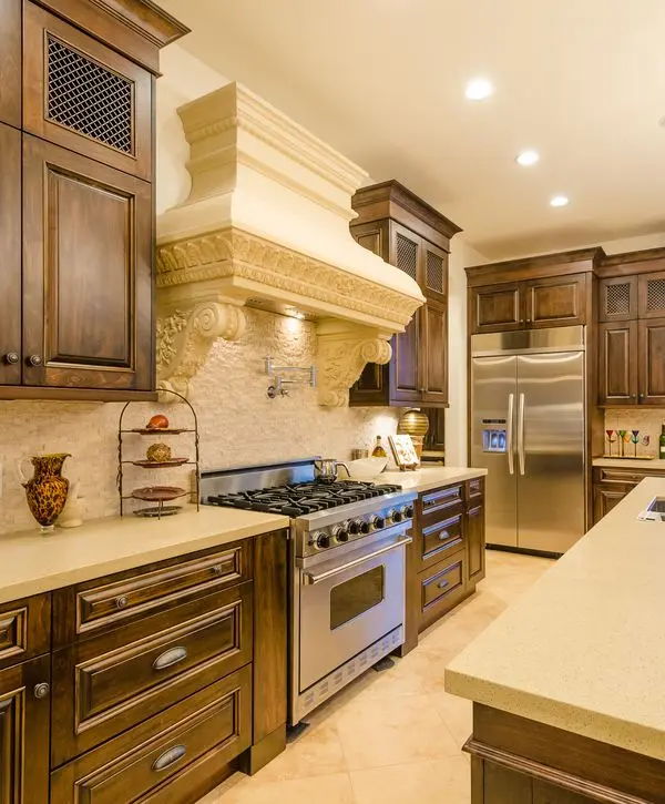 A luxury kitchen featuring dark wood custom cabinetry, an ornate stone range hood, and professional stainless steel appliances installed during a kitchen remodeling in Old Bridge, NJ.