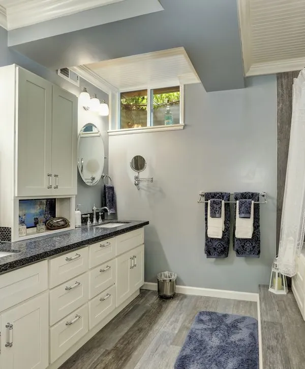 A recently finished basement bathroom remodeling in Keyport, NJ, featuring white shaker cabinets, dark granite countertops, and grey wood-look flooring.