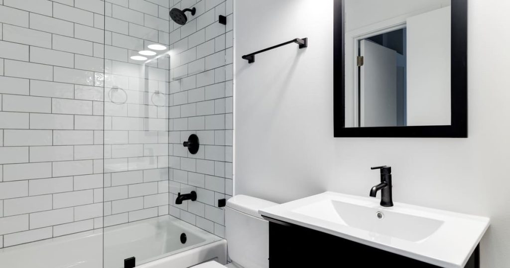 A modern bathroom featuring professional tile waterproofing behind white subway tiles in a walk-in shower with matte black hardware.