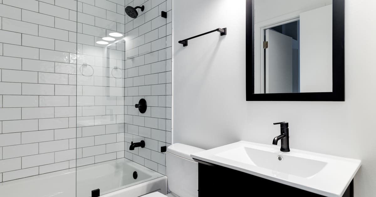 A modern bathroom featuring professional tile waterproofing behind white subway tiles in a walk-in shower with matte black hardware.