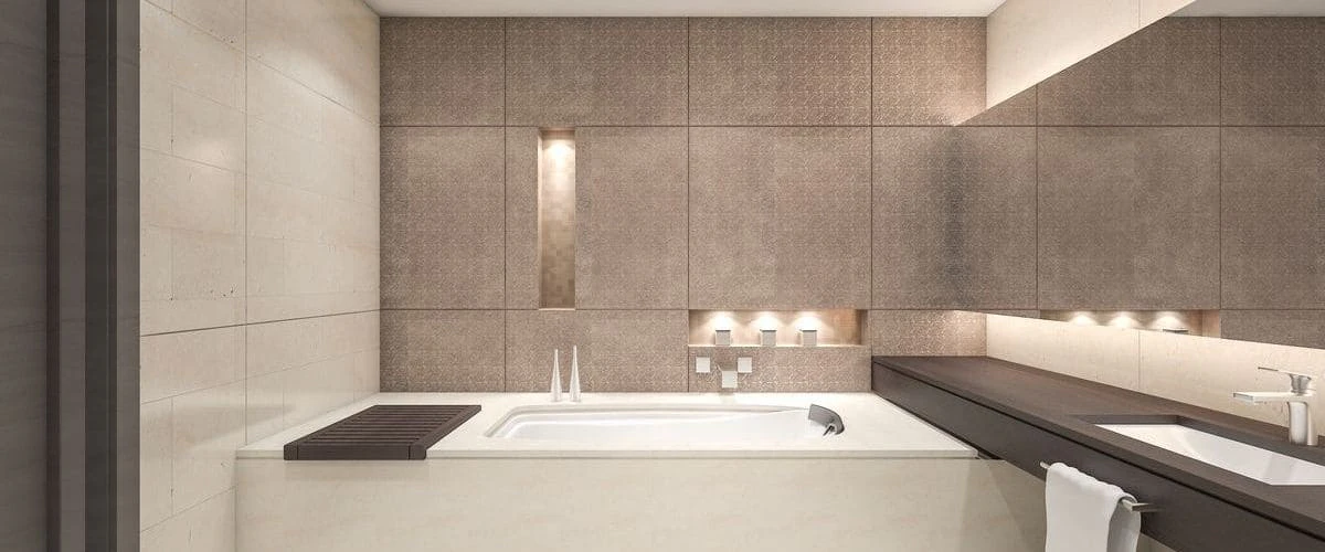 A sleek, modern bathroom featuring a built-in white rectangular bathtub, neutral textured stone wall tiles with warm integrated accent lighting, and a dark wood vanity counter.