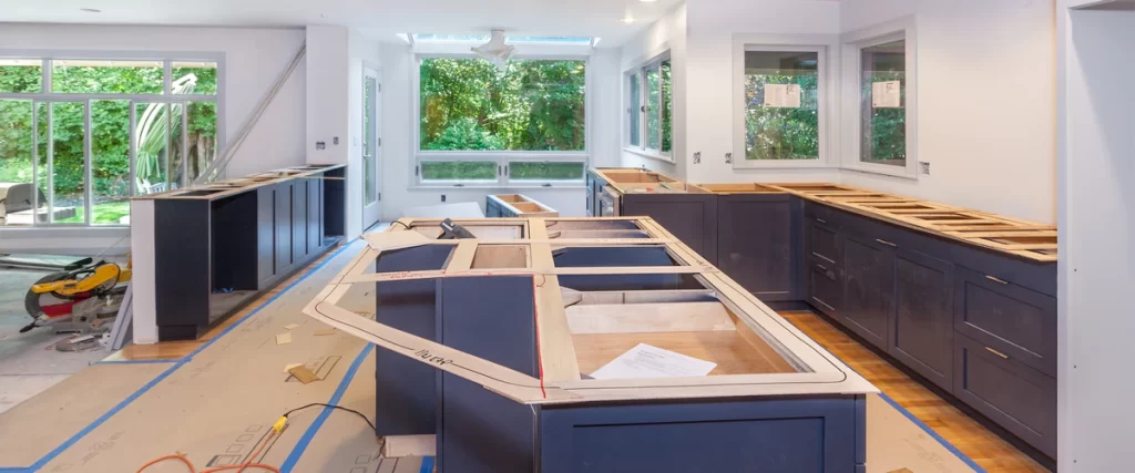 A kitchen mid-renovation with new navy blue lower cabinets installed and a large central island frame being prepped for countertops.