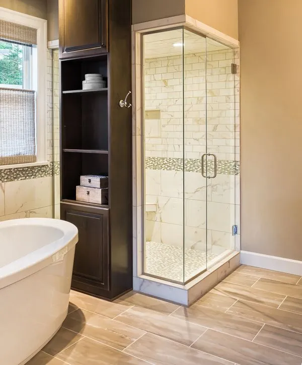 A modern bathroom remodeling in Union Beach, NJ featuring a frameless glass walk-in shower with marble subway tile and a tall dark wood storage cabinet.