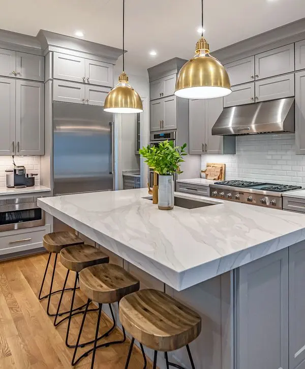 Luxury kitchen remodeling in Red Bank, NJ featuring light gray cabinetry, a white marble waterfall island, and gold pendant lighting.