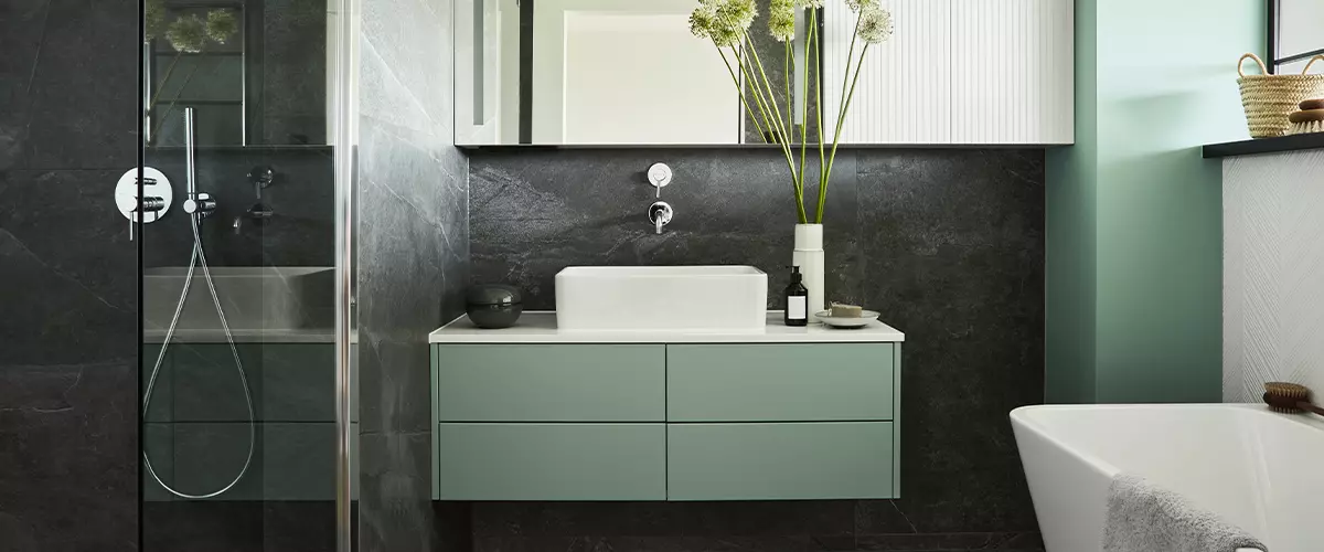 Contemporary bathroom design highlighting a sage green floating vanity with a white vessel sink against a dark charcoal stone-textured accent wall.