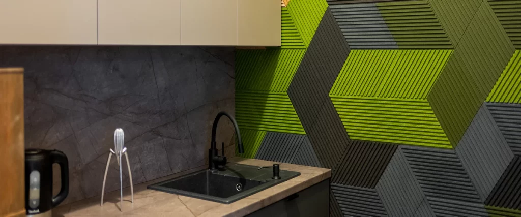 Close-up of green and grey textured 3D geometric acoustic wall panels installed next to a kitchen sink to absorb kitchen noise.