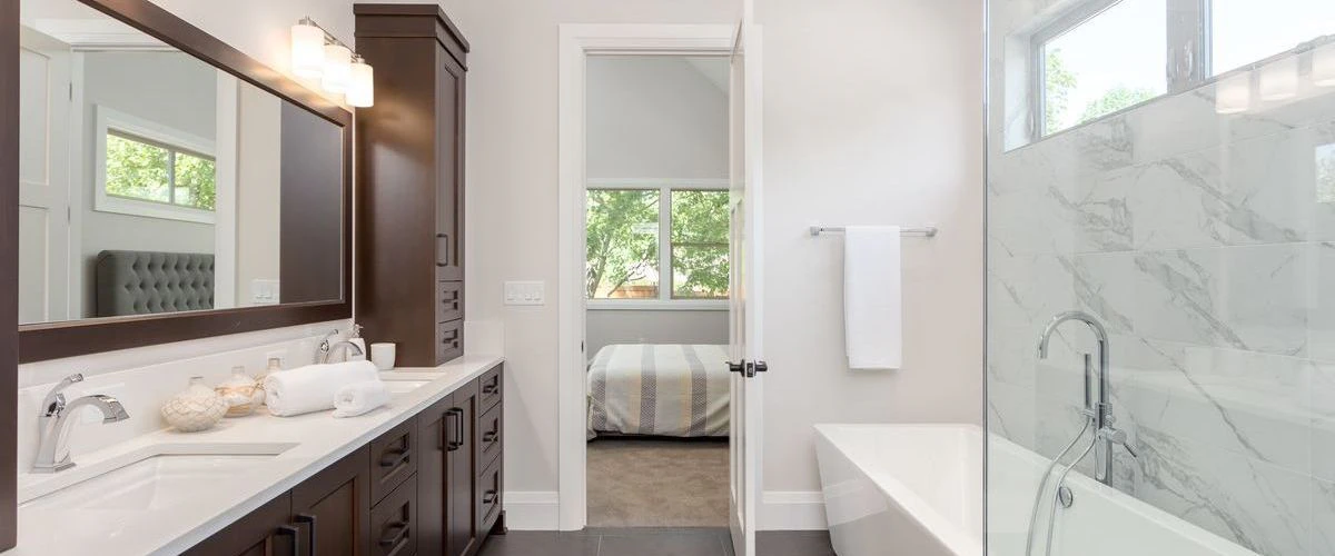 Modern bathroom interior showcasing a dark wood vanity with white rectangular sinks and a walk-in shower with elegant marble wall tiles.