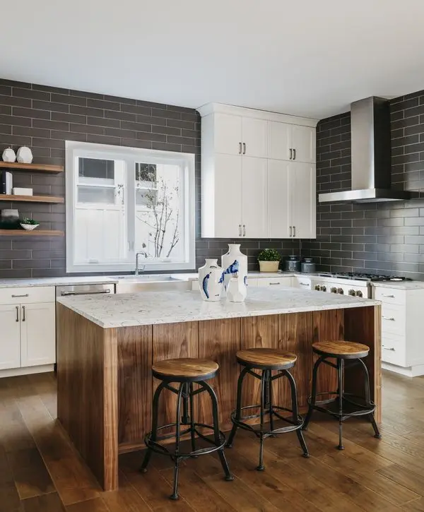 Modern kitchen remodeling in Manalapan Township, NJ featuring a custom wood-paneled island with three stools, white countertops, a dark gray subway tile backsplash, and white upper cabinets.