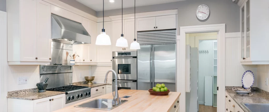 A bright, modern kitchen featuring white cabinetry, a large wood-top island, and high-end stainless steel appliances including a double oven and refrigerator.