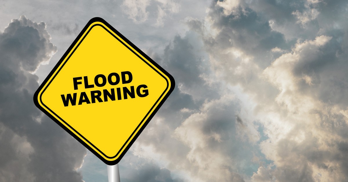 A yellow diamond-shaped flood warning sign against a backdrop of dark, dramatic storm clouds for Port Monmouth flood zone remodeling.