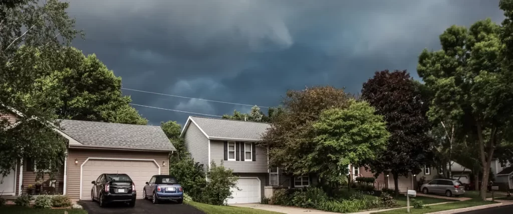 Dark, heavy storm clouds looming over a row of suburban residential houses and parked cars, reminiscent of conditions during Hurricane Sandy.