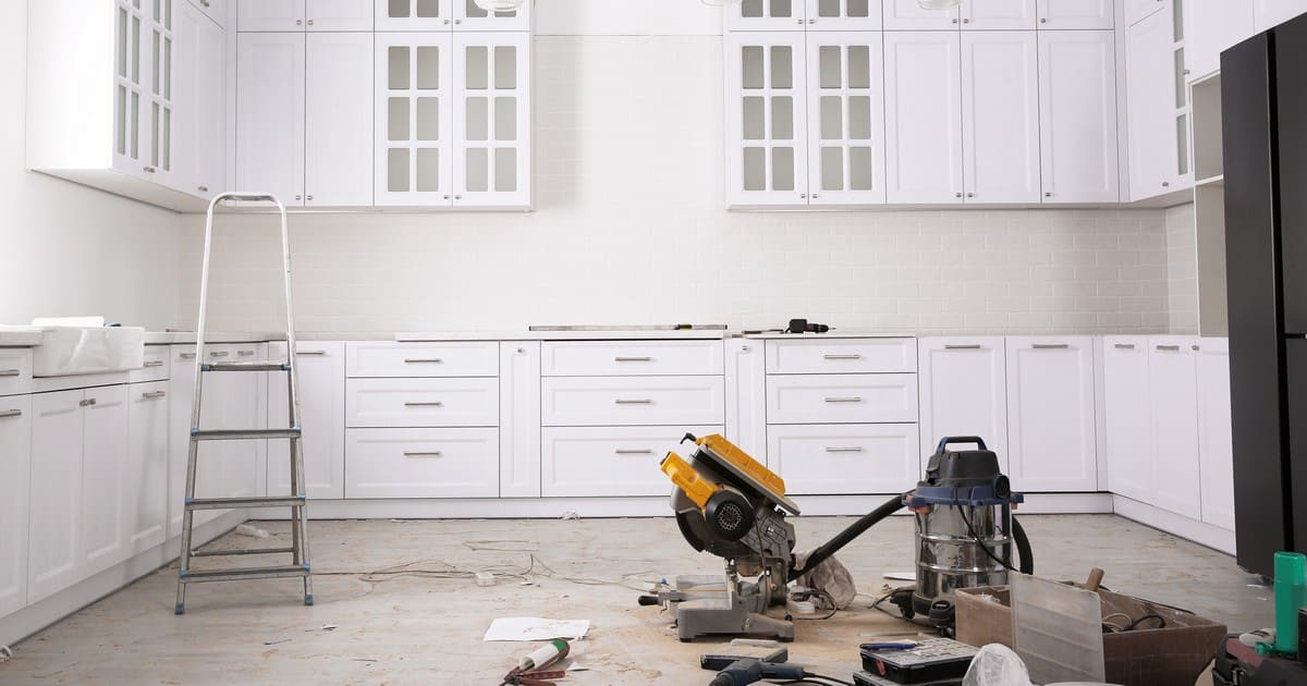 A white kitchen expansion in Matawan under construction showing installed shaker cabinets, a miter saw, and a shop vac on a dusty floor during a permitted renovation.