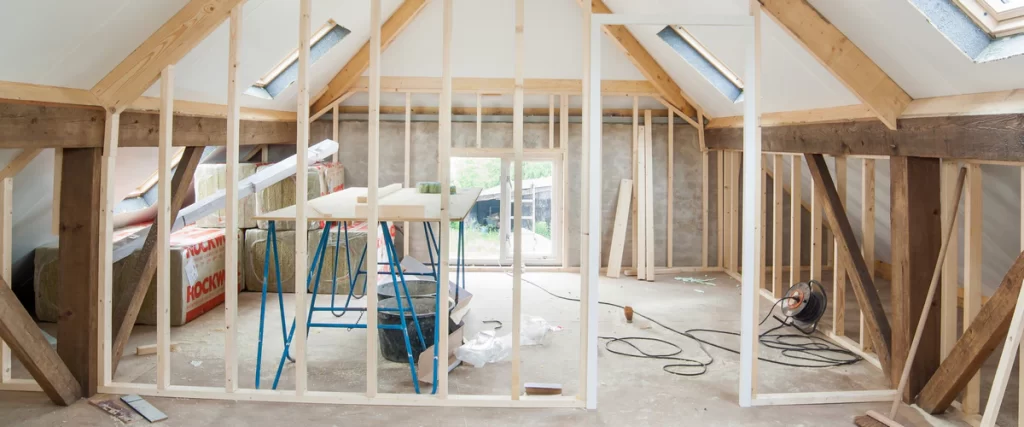 Interior view of an attic renovation showing new wood framing, installed skylights, and insulation bundles indicating a major structural change.
