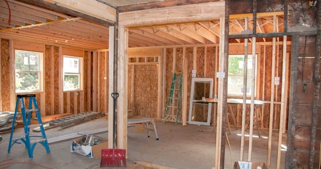 Interior of a house under heavy construction showing exposed wooden studs, a blue ladder, and a red shovel on the floor after removing load bearing wall NJ.