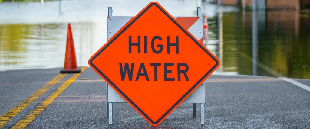 Orange high water warning sign blocking a flooded street in a high-risk flood zone area.