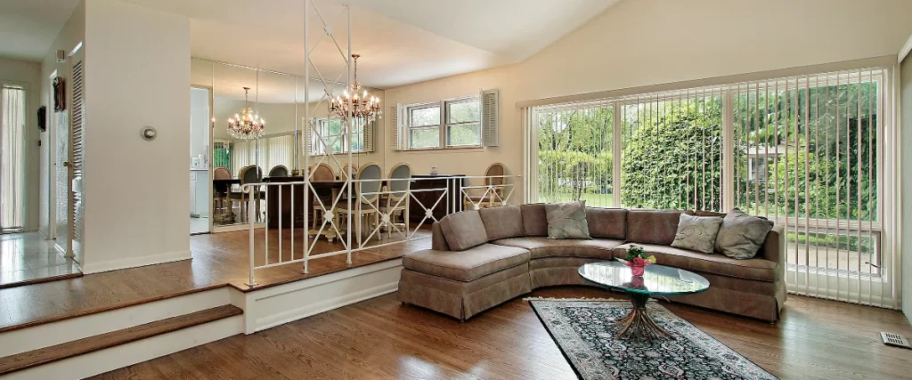 Interior view of a classic split level home featuring a step-down living room with a curved sofa and an elevated mirrored dining area.