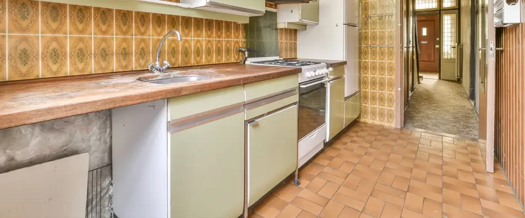 Outdated kitchen before remodel with vintage cabinets, worn countertops, and retro tile backsplash
