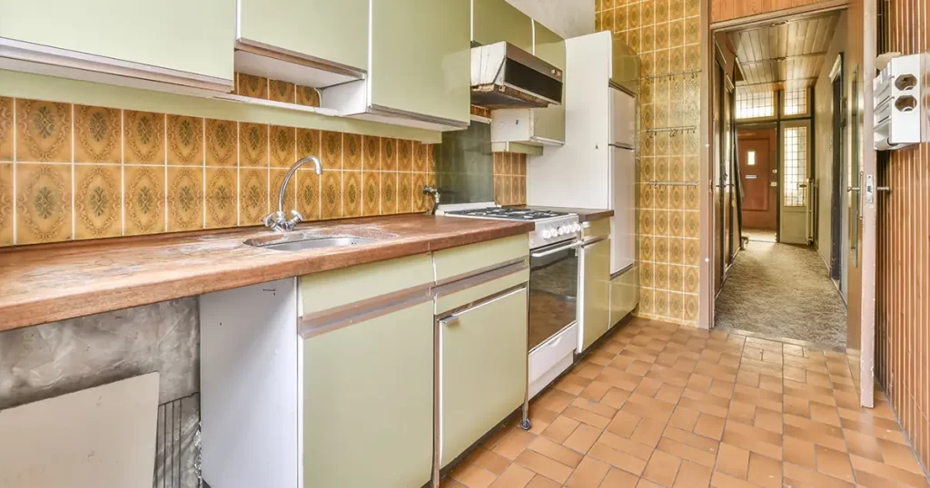 Outdated kitchen before remodel with vintage cabinets, worn countertops, and retro tile backsplash
